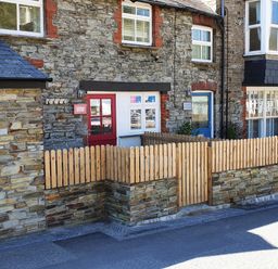 Stone exterior of a building with a red door and blue door with wooden picket fences in front at Beach Hut in Trebarwith Strand