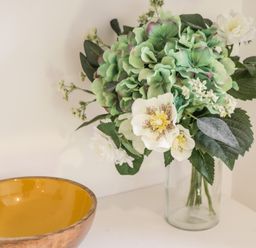 A glass vase with green and white flowers on a white surface next to a wooden bowl with a yellow interior at West Cliff Apartment Whitby