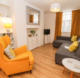 A living room with an orange armchair gray sofa a small white table and a TV on a stand at West Cliff Apartment in Whitby