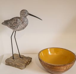 A wooden bird sculpture on a stand next to a wooden bowl with a yellow interior at West Cliff Apartment in Whitby