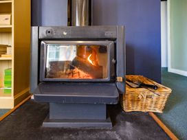 A wood stove with firewood in a basket at Oroua Cottage - Rangataua Bach Ohakune