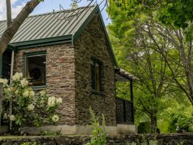 A stone cottage with a balcony and flower bushes at Tranquil Tipperary - Arrowtown Holiday Home Arrowtown
