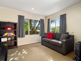 A small sitting room with a gray sofa and colorful cushions a dark wooden bookshelf with toys and two windows with gray curtains at Lakewood Haven - Taupo Holiday Home in Rainbow Point