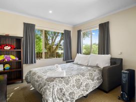 A bedroom with a bed sofa covered with patterned bedding next to two windows and a wooden shelf with stuffed toys at Lakewood Haven - Taupo Holiday Home in Rainbow Point