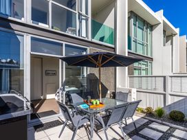 An outdoor patio with a glass table and umbrella surrounded by chairs next to a sliding glass door at 24 Marina View Retreat  Taupo Holiday Apartment in Taupo Bay