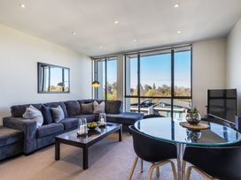 A living room with a dark sectional sofa a coffee table with candles a glass dining table with chairs and large windows at 24 Marina View Retreat - Taupo Holiday Apartment Taupo Bay