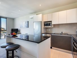 A kitchen with a black countertop island with two stools a refrigerator microwave and a sink at 24 Marina View Retreat - Taupo Holiday Apartment Taupo Bay