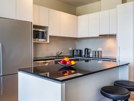 A kitchen with white cabinets black countertops a stainless steel refrigerator microwave toaster kettle and a bowl of fruit on the island at 24 Marina View Retreat - Taupo Holiday Apartment in Taupo Bay