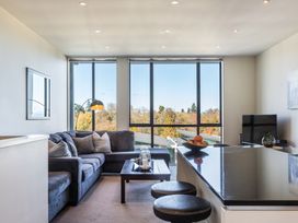 A living room with a sectional sofa coffee table floor lamp and kitchen counter with stools overlooking trees at 24 Marina View Retreat Taupo Bay