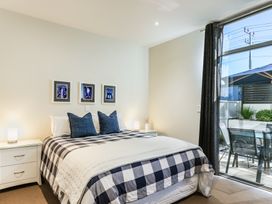 A bedroom with a bed covered in checkered bedding two blue pillows bedside tables lamps and framed pictures on the wall at 24 Marina View Retreat - Taupo Holiday Apartment in Taupo Bay