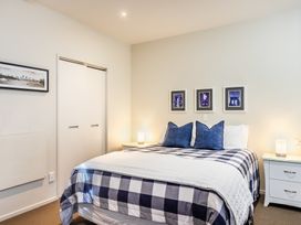 A bedroom with a bed with checkered bedding and blue pillows beside two white nightstands with lamps at 24 Marina View Retreat - Taupo Holiday Apartment in Taupo Bay