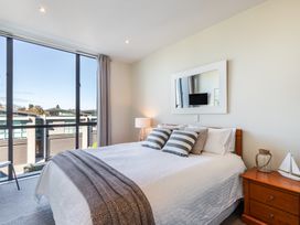 A bedroom with a bed with striped pillows a bedside table with a lamp and a sailboat model and a large window showing adjacent buildings at 24 Marina View Retreat - Taupo Holiday Apartment Taupo Bay
