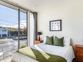 A bedroom with a bed two green pillows a green throw two wooden nightstands a black lamp large windows and a framed leaf artwork at 24 Marina View Retreat - Taupo Holiday Apartment in Taupo Bay