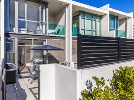 An outdoor patio with chairs and a table under an umbrella outside a modern apartment with large windows at 24 Marina View Retreat Taupo Bay