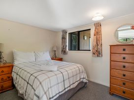 A bedroom with a bed folded towel on it two bedside tables with lamps a window with curtains and a wooden dresser with a mirror at Acacia Views - Acacia Bay Holiday Home in Acacia Bay