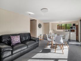 A living room with a black leather couch and a glass dining table with white chairs at Acacia Views - Acacia Bay Holiday Home in Acacia Bay