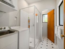 A laundry room with a washing machine a laundry sink a shower and an open door leading to a toilet at Acacia Views - Acacia Bay Holiday Home in Acacia Bay