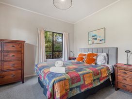 A bedroom with a bed with colorful bedding two orange pillows two rolled white towels on the bed wooden chest of drawers and bedside tables at Acacia Views - Acacia Bay Holiday Home in Acacia Bay