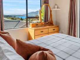 A bedroom with a bed and pillows next to a wooden dresser with an oval mirror and window showing a mountain and water view at Acacia Views - Acacia Bay Holiday Home in Acacia Bay