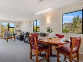 A dining area with a round wooden table set for four and a living room with two black leather sofas and an armchair at Acacia Views - Acacia Bay Holiday Home in Acacia Bay