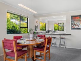 A dining area with a wooden table and red cushioned chairs and a kitchen counter with three metal bar stools at Acacia Views - Acacia Bay Holiday Home in Acacia Bay