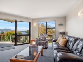 A living room with a leather sofa, patterned armchair, glass top coffee table, and sliding glass door leading to a balcony at Acacia Views - Acacia Bay Holiday Home in Acacia Bay