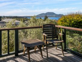 A wooden chair and table on a deck overlooking trees water and mountains at Acacia Views - Acacia Bay Holiday Home in Acacia Bay