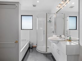 A bathroom with a bathtub a glass shower cubicle a sink with cabinets and a large mirror at Acacia Views - Acacia Bay Holiday Home in Acacia Bay