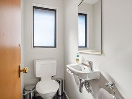A small bathroom with a toilet a sink a mirror a window a towel rack and a wooden door at Acacia Views - Acacia Bay Holiday Home in Acacia Bay