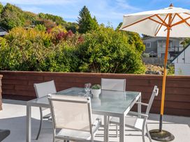 An outdoor patio with a glass table, four chairs, a white umbrella, and greenery in the background at Acacia Views - Acacia Bay Holiday Home in Acacia Bay