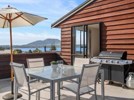 An outdoor patio with a glass table and four chairs a barbecue grill and an umbrella with a lake and mountain view at Acacia Views - Acacia Bay Holiday Home in Acacia Bay