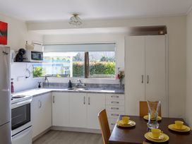 A kitchen with stove, sink, cabinets and dining table at Ronas - Whiritoa Beach Bach Whiritoa Beach