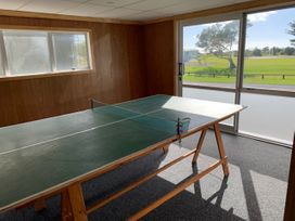 A room with wood-paneled walls and a green table tennis table near a large window with a view of grass and trees at Mollies Place - Waihi Beach Holiday Unit in Waihi Beach