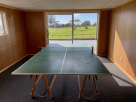 A room with wood panel walls a ping pong table and a large window overlooking a grassy field at Mollies Place Waihi Beach
