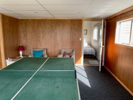 A room with a ping pong table two chairs with pillows a side table with a lamp and an open door showing a bedroom at Mollies Place - Waihi Beach Holiday Unit in Waihi Beach