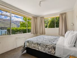 A bedroom with a bed and windows showing mountains and a lake at Lakeside Serenity - Wanaka