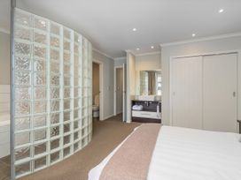 A bedroom with a glass block wall and attached bathroom at Putt it at Pauanui - Pauanui