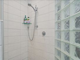 A shower with shelf and bottles at Putt it at Pauanui - Pauanui Holiday Home