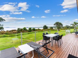 An outdoor deck with seating and a table overlooking a lake at Beachfront Escape - Snells Beach Holiday Home in Matakana
