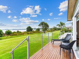 An outdoor area with a deck and chairs overlooking a grassy area and water at Beachfront Escape - Snells Beach Holiday Home in Matakana
