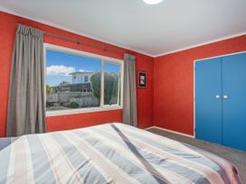 A bedroom with a bed, window, and blue doors at Nest by the Beach - Cooks Beach
