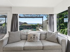 A living room with a sofa and windows overlooking the garden at Wharewaka Bach - Lake Taupo Holiday Home Wharewaka