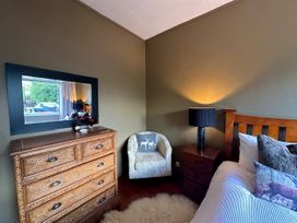 A bedroom with a dresser, lamp, armchair, and bed at Stag & 3 Pigs - Ohakune