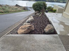 An outdoor area with rocks, mulch, and a concrete pathway at Kotare Point Paradise - Akaroa