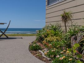 An outdoor area with a table and flowers next to the ocean at Beachfront Beauty - Whangamata Beachfront Home Whangamata