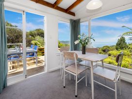 A dining area with a table and chairs next to large windows overlooking greenery and ocean at Piha City Escape Piha Holiday Home in Piha