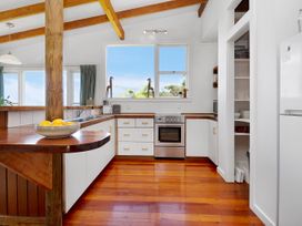 A kitchen with wooden floors white cabinets a stainless steel stove and a bowl of lemons on the counter at Piha - City Escape Piha Holiday Home in Piha
