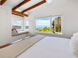 A bedroom with a bed near large windows showing a view of trees and hills at Piha City Escape Piha Holiday Home Piha