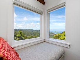 A corner seating area with cushions and large windows showing a view of hills and ocean at Piha City Escape Piha Holiday Home
