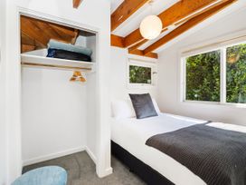 A bedroom with a bed near windows and an open closet with hangers at Piha - City Escape Piha Holiday Home Piha